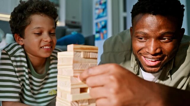 Father son playing block tower game home. Close up dad pulling wooden brick.