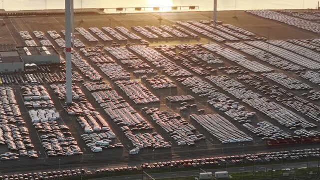 Aerial drone view of thousands of new import export cars parked in a sea port terminal. Commercial automotive supply chain and maritime freight logistics.