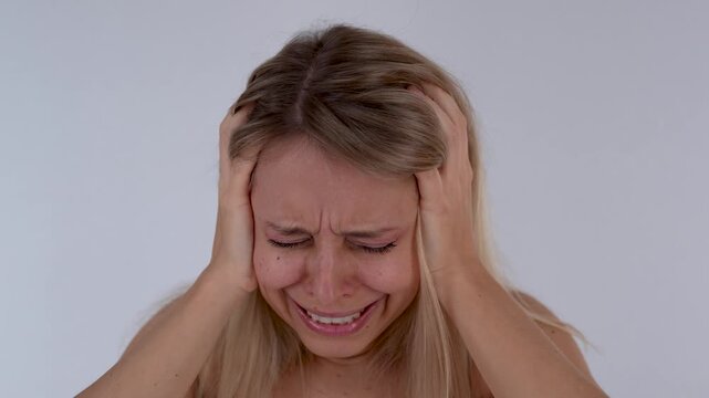 Young blonde woman holding her head in shock and psychological distress, showing fear, panic, horror and emotional instability