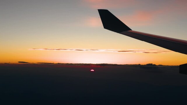 Red sun rises above the haze under streaks of clouds and a pink sky behind the dark wing tip of an airliner descending toward Sao Paulo in Brazil