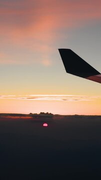 Vertical video of a small red sun rising through haze at dawn below a golden band of sky and the dark winglet of an airliner near Sao Paulo Brazil