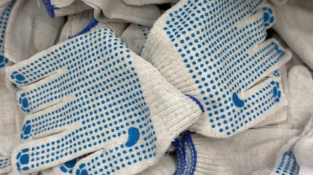 White cotton construction gloves with blue rubber dots are piled together. Work safety wear, protective equipment, industrial hand protection.