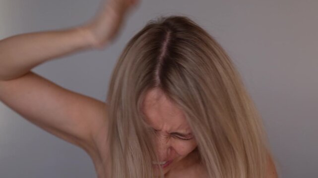 Young blonde woman strikes her head in visible anguish, expressing self-directed frustration, emotional instability and a distressed meltdown during an intense inner conflict