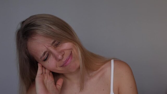 Young blonde woman tilts and shakes her head while pressing her ear with one hand, reacting to an uncomfortable blocked sensation, ear pressure and possible hearing difficulties