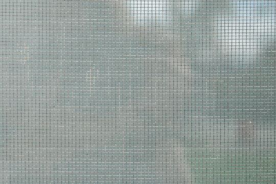 Metal window screen mesh with fine grid pattern, soft focus background, neutral color, closeup geometric texture for modern architectural or protective design. Real photo