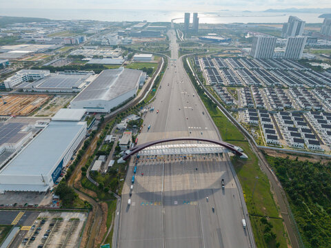 Simpang Ampat, Malaysia - 05 October 2026: Aerial view of Plaza Tol Bandar Cassia, a modern toll plaza with an arched roof spanning a highway near industrial warehouses and residential areas.