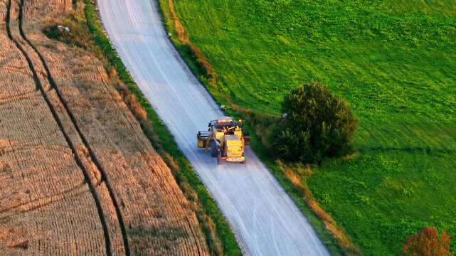 Valmiera, Latvia - 14 August 2026: Aerial view of a combine harvester driving on a rural dirt road between a golden wheat field and a lush green field in the countryside.
