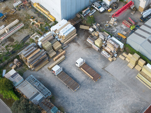 Melbourne, Australia - 06 October 2026: Aerial view of an industrial yard with flatbed trucks, stacks of timber and construction materials, and warehouse buildings in the Knox and Bayswater area.