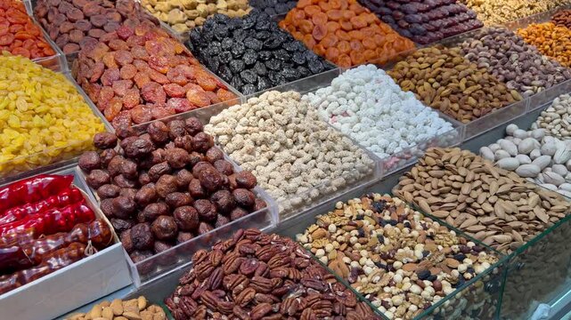 Wide variety of dried fruits, almonds, pistachios, and sugar coated nuts at market stall. Healthy snack selection, organic nuts assortment, middle eastern bazaar food, supermarket retail display.
