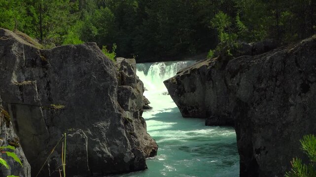 Close-up stationary view of a waterfall on the turquoise Cheakamus River rushing through a rugged stone canyon near Whistler, British Columbia. Glacial waters churn past dark volcanic rocks.