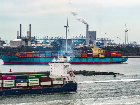 Europoort Rotterdam, Netherlands - 16 August 2026: Aerial view of container ships in the industrial port of Europoort Rotterdam with wind turbines and smoke stacks.