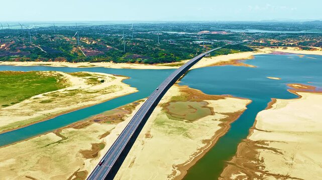 High angle aerial view shows a long highway bridge spanning across Poyang Lake during dry season, surrounded by sandbanks and wind turbines.
