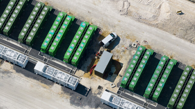 Saleux, Hauts-de-France, France - 08 July 2026: Aerial view of a battery energy storage system with rows of green containers, white cooling units, a white van, and workers.