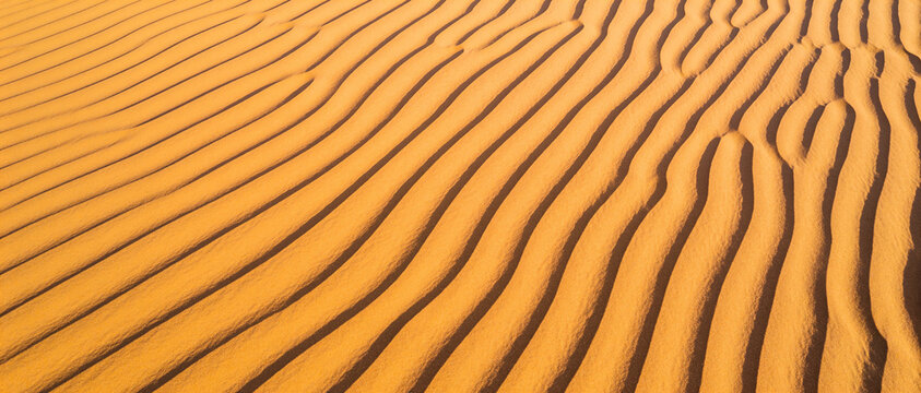 Close-up of sand with wavy parallel ripples in golden-orange tones, seen from above.