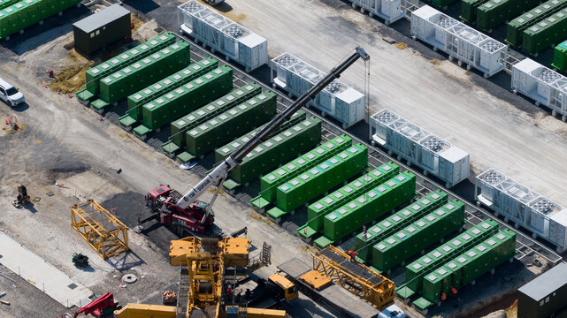 Saleux, Hauts-de-France, France - 08 July 2026: Aerial view of a construction site featuring rows of green modular battery storage units, a mobile crane, and various industrial equipment.