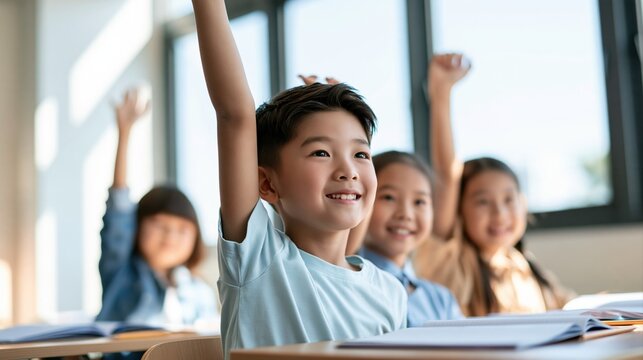 smiling asian schoolboy raising his hand to answer a question during lesson in bright classroom with eager classmates and open notebooks