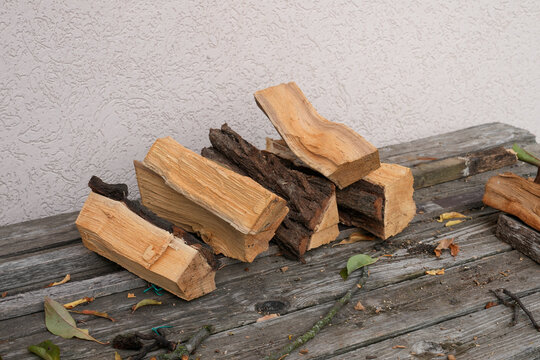 Split firewood stacked on weathered wooden bench beside plaster wall. Rustic fuel supply for home heating guides and countryside living content. Real Photo