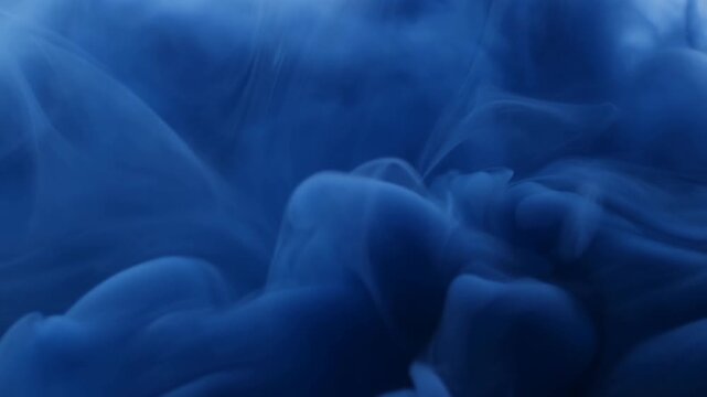 Blue ink pigment curls and diffuses through water in layered abstract swirls