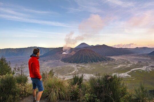 Young man in front of volcanic landscape at sunset, view in Tengger Caldera, smoking volcano Gunung Bromo, in front Mt. Batok, in the back Mt. Kursi, Mt. Gunung Semeru, National Park Bromo-Tengger-Semeru, Java, Indonesia