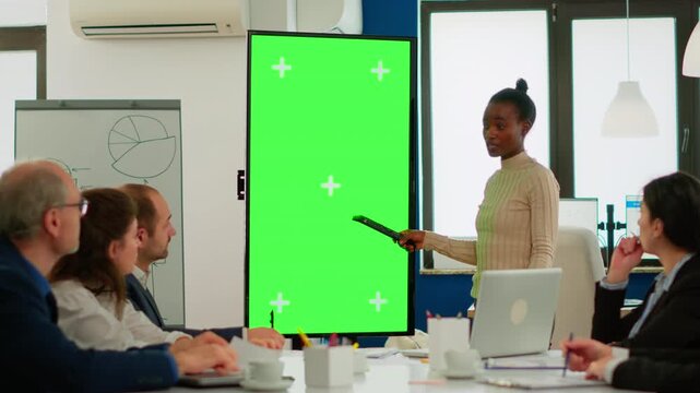 Greenscreen, teamwork and presentation with businesswoman gesturing toward a chroma key monitor while colleagues listen, for strategy briefing, project planning, collaboration and custom media.