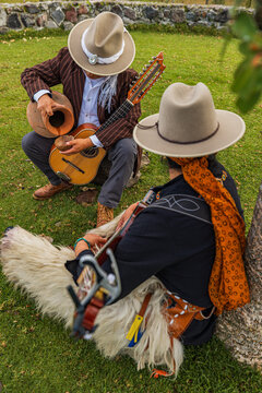 Traditional indigenous musicians wearing chaps playing guitar in scenic Andean landscape