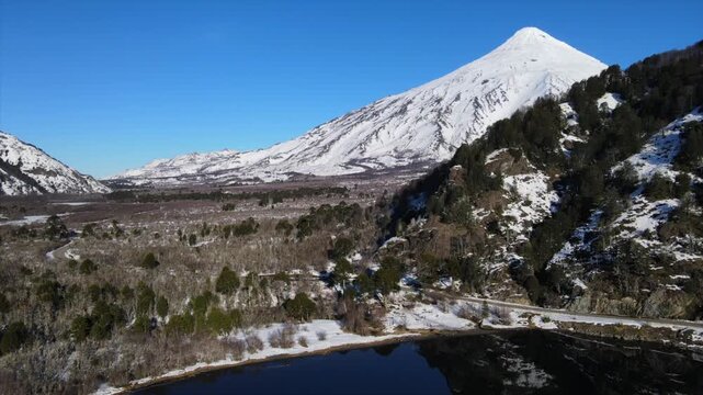 Vista a&eacute;rea de drone del majestuoso volc&aacute;n Lan&iacute;n, sobrevuelo sobre el bosque nevado en Patagonia y laguna Quillehue.