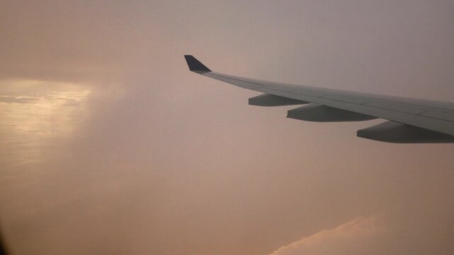 Airliner wing glides through a soft golden haze above layers of clouds with light reflecting on the cloud tops during a hazy morning flight north of Sao Paulo Brazil