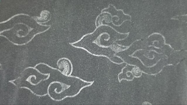 A close-up shot showing the traditional Indonesian Mega Mendung cloud motif drawn with subtle white outlines on a dark textured background