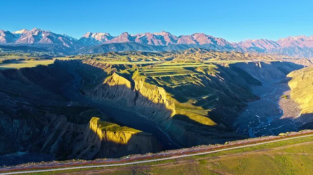 Panoramc wide angle view shows Anjihai Grand Canyon with dramatic cliffs, riverbed and snowcapped mountains in Xinjiang, China.