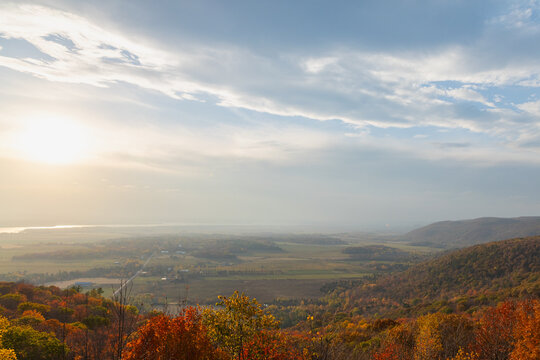 High angle autumn mountain vista with bright sun and cloud sky over valley. Champlain Lookout in Gatineau Park, Canada.