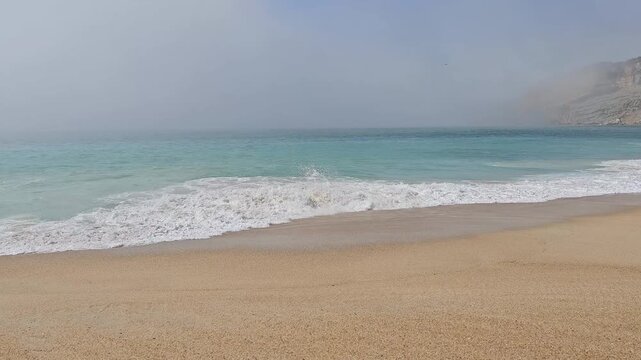 Big ocean waves crashing with heavy fog and cliffs visible in distance in Nazar&eacute; Portugal