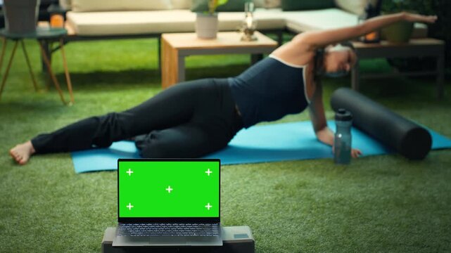 Laptop with a blank green screen in landscape orientation sits against a blurred rooftop, providing editable display space for content and advertising.