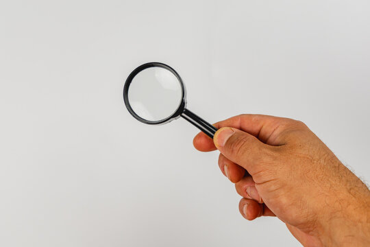 Hand holding a magnifying glass above a plain background for inspection