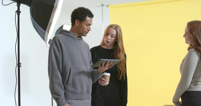 Diverse coworkers consulting tablet, pointing at shots, testing handset, coordinating studio shoot