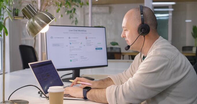 Man responding to Live Chat Workflow, typing at desk and pointing, headset on, resolving issue