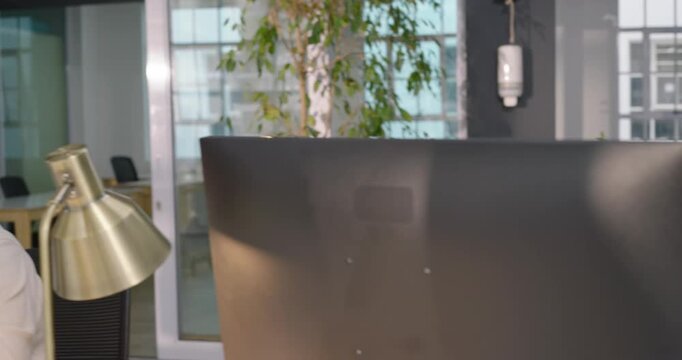 Diverse coworkers taking new calls at shared desk row, typing, adjusting headsets, helping clients