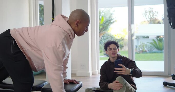African American men at home gym, man doing one-arm dumbbell rows on bench checking phone timer