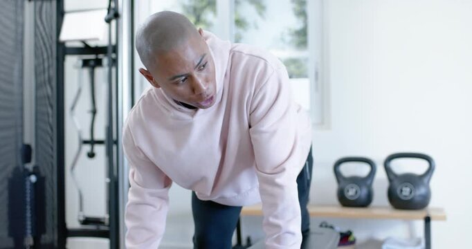 African American men, trainer cueing client in pink hoodie doing one-arm hex dumbbell rows on bench