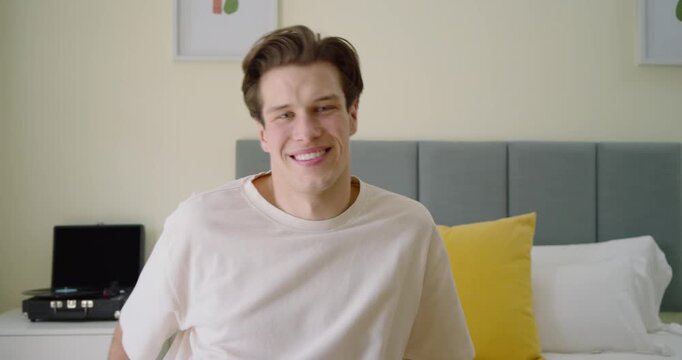 Man in tee on bed, shifting and smiling with camera moving, looking toward garden catching light