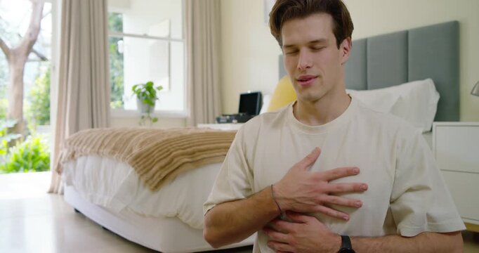 Adult man sitting on mat in bedroom wearing watch, starting meditation by breathing deeply to calm