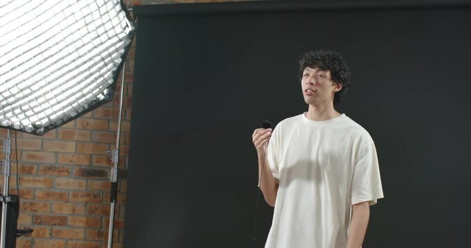 Male host and crew on set holding lav mic speaking, walking behind adjusting softbox fixing light