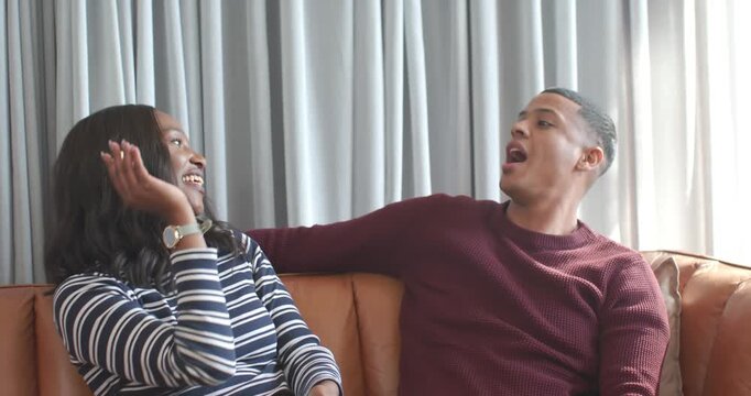 African American couple laughing, woman tossing popcorn after man reaching for glass bowl on sofa