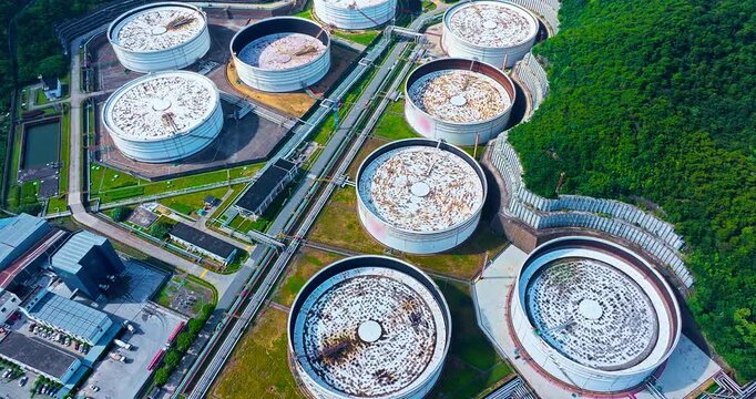 High angle view of large white oil storage tanks and industrial pipeline infrastructure situated near lush green hills.