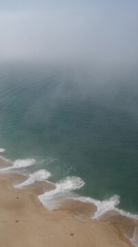 Fog rolling in over Praia do Norte in Nazar&eacute; Portugal with large ocean waves view from high overlook vertical video
