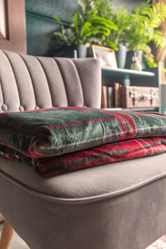 Green red tartan fleece blanket throw folded on a grey chair in a dark green and gold room, with sunlight shining into the room.