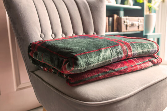 Green red tartan fleece blanket throw folded on a grey chair in a dark green and gold room, with sunlight shining into the room.
