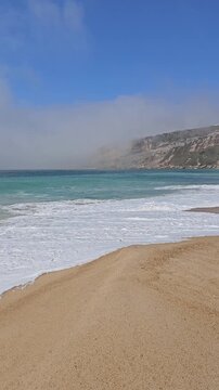 Big ocean waves crashing with heavy fog and cliffs visible in distance in Nazar&eacute; Portugal vertical video