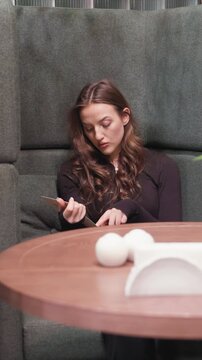 Woman is seated on green cushioned bench in what appears to be casual dining area. Woman holds object possibly food or utensil and interacts with it at table