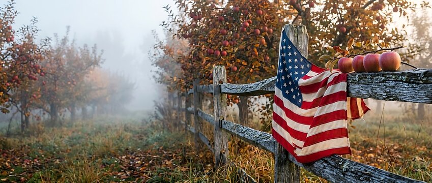 American Veterans Day American flag draped over wooden fence in misty orchard with ripe apples on branches