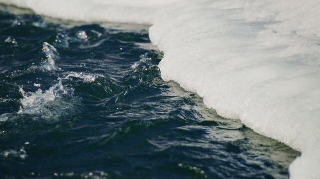 Deep blue water churns beside melting white ice. Icebergs slowly break apart into frothy waves. Cold water crashes against snow-covered cliffs. Nature's power reshapes frozen landscapes with each wave